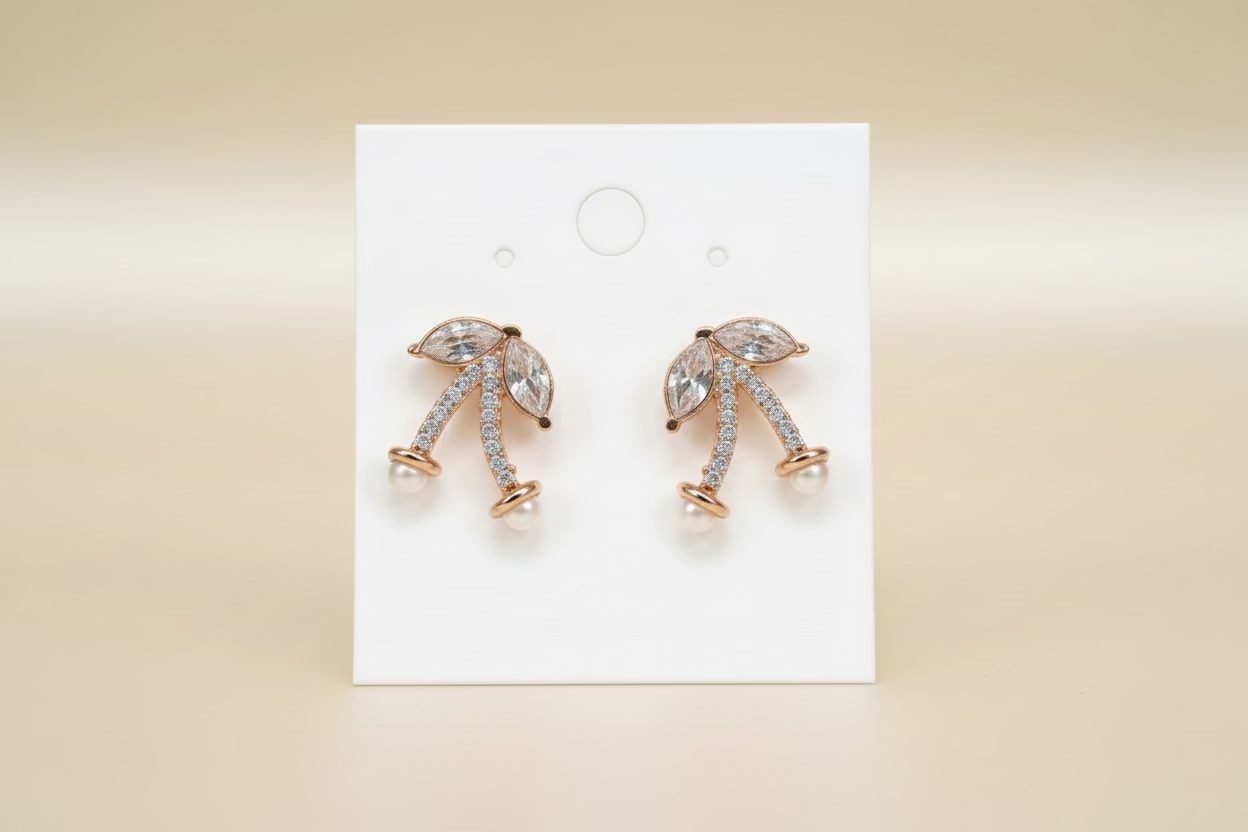 Rose gold earrings with dangling elements on a white card against a beige background